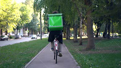 Delivery man with green backpack rides a bicycle through the city with food delivery