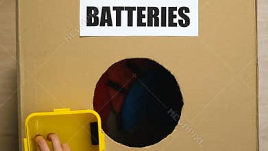 Hand throwing batteries in box with clothes on bottom, inappropriate sorting