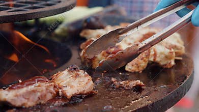Cook is turning different kind of meat on grill plate