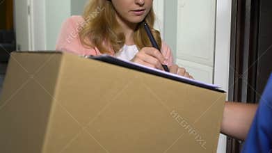 Attractive lady accepting parcel in cardboard box and signing documents delivery