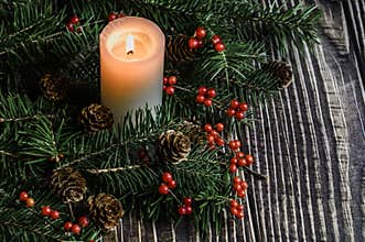 Christmas tree, red berries and burning white candles on a table