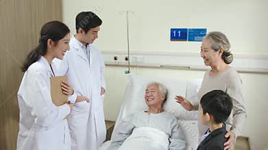Asian doctors talking to senior patient and family members in hospital ward
