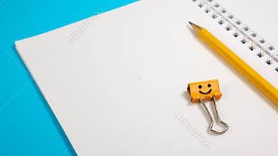 School Notepad with Yellow Pencil and Orange Smile Binder Clip on Blue Background