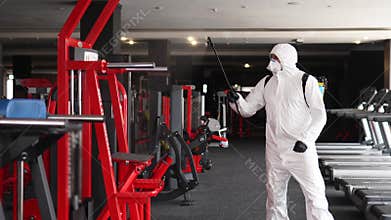 Hazmat worker disinfects gym fitness equipment from coronavirus covid-19 hazard with antibacterial sanitizer sprayer on