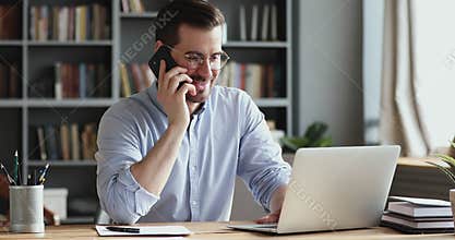 Smiling business man using laptop talking on phone in office