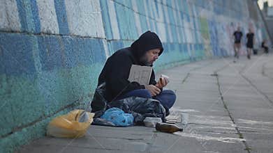 homeless poor young man sitting on the ground in the city with a Help table while asking for money to survive. Eating