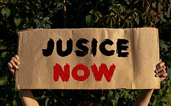 A poster with the words JUSICE NOW in the hands of a young girl on a background of green foliage