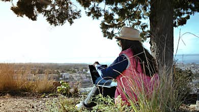 Solitude and Creativity: Female Author Sitting on a Mountain, Gazing into the Distance, and Writing Thoughtfully on a
