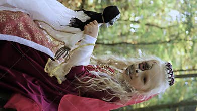A child girl sits on a stump in the forest in a medieval dress in the form of a dead princess with makeup on her face