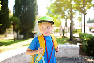 Elementary boy wearing baseball cap with backpack and name badge on his neck goes to school. Child is waiting of school bus. Kids