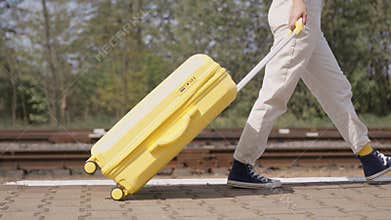 Young woman walks cheerfully and confidently along railway platform carrying yellow suitcase, tuned in to explore new