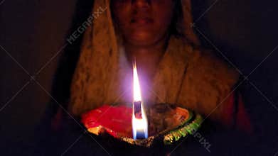 Woman holding and illuminating brightly burning clay Diya or clay oil lamp, close up Macro shot.