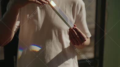 Man holding triangular glass prism, refracting sunlight and creating rainbow effect, showcasing principles of optics and