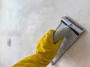 Construction worker sanding wall with sandpaper holder and wearing yellow gloves