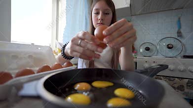 teenage girl cooking fried eggs in kitchen.