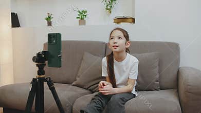 Young girl participates in virtual meeting from home while seated on a cozy couch with plants in the background