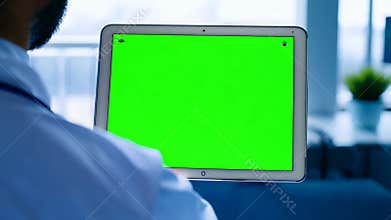 Medical professional holding digital tablet with green screen display, standing in modern clinic setting for healthcare technology