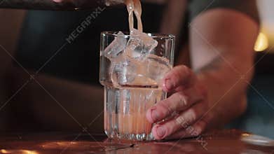 The bartender pours white coctail Tequila Sunrise into a glass with ice. Close-up