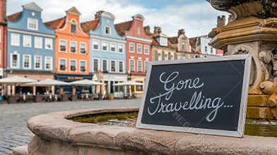 Charming cobblestone square with a \'Gone Travelling\' sign in front of colorful buildings