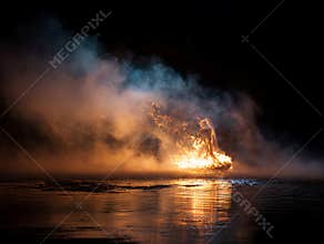 Fire engulfing a boat on still water, smoke forming a human figure over the flames Dark background contrasts with the intense glow