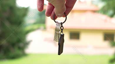 Home keys with wooden house shaped keychain against background of new bungalow