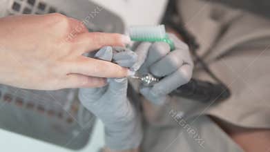 Slow motion close-up of a nail technician performing an electric manicure with a nail drill.
