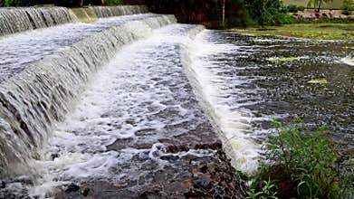 Flood water flows over a canal weir after heavy rains