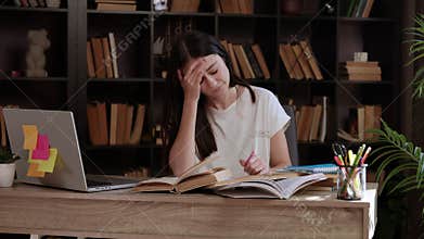 Tired student at a desk in a beautiful library, her head and eyes aching from reading and studying. The young woman