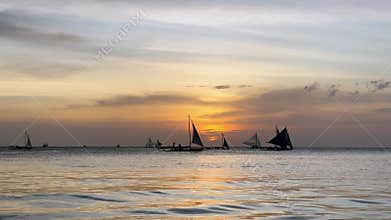 Traditional sailboats at sunset on the calm ocean waters