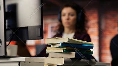 Stack of books on startup office desk in front of woman working, closeup