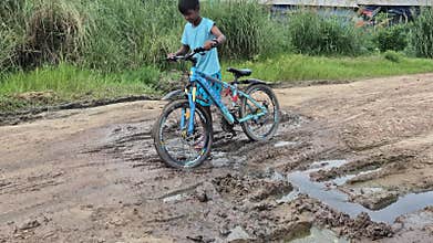 Boy Pushing Bicycle On Muddy Rural Road In Bangladesh