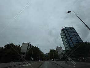 Rainy city street with modern glass tower, cyclist, wet road, overcast sky