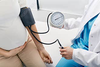 Doctor measuring blood pressure of pregnant woman on maternity leave while visit by perinatal center. Examinations during