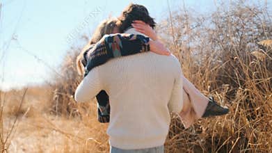 Man romantically carries woman during a walk in autumn grass field.