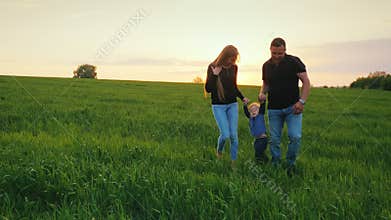 A happy couple of parents with a small son are walking across the field towards the sunset. Happy family with a child
