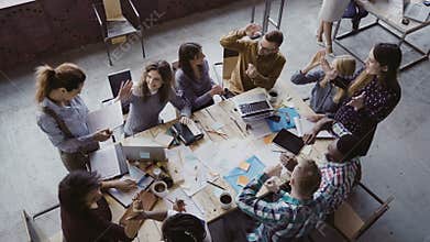Top view of creative business team working at modern office. Colleagues talking, smiling, high five with each other.