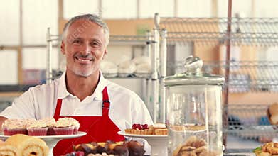 Happy server looking at camera with thumbs up behind cakes