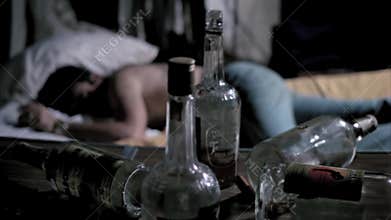 Empty liquor bottles on table with man sleeping in background