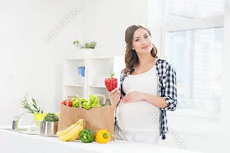 Beautiful pregnant smiling woman in the kitchen eating vegetables