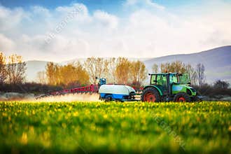Farming tractor plowing and spraying on the green field