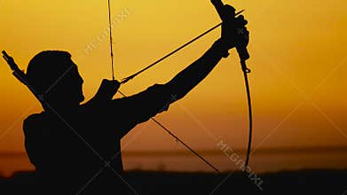 Archery silhouette, sun sets behind the archer. Young hunter.