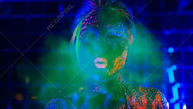 Girl in ultraviolet light blows green fluorescent powder with palm