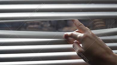 Woman looking through the blinds of the window to the street