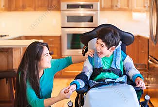 Disabled boy in wheelchair laughing with teen sister in kitchen