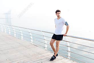 Man athlete with armband and cell phone standing on pier