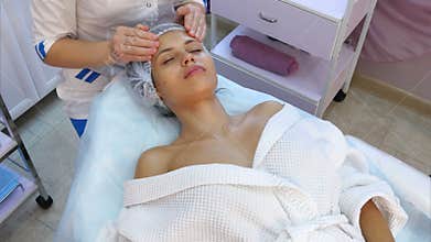 Beautiful young woman receiving facial massage with closed eyes in a spa salon.