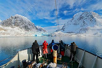Holiday travel in Arctic, Svalbard, Norway. People on the boat. Winter mountain with snow, blue glacier ice with sea in the foregr