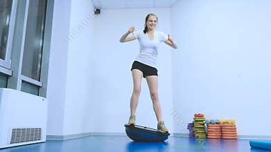Young smiling girl keep the balance on the simulatur bosu in the gym