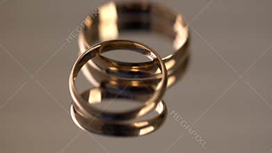 Two golden wedding rings rotating on mirror surface