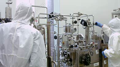 Scientists in protective suits working on vat